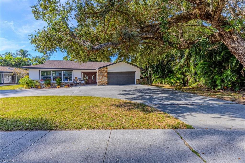 Ranch-style home featuring stone siding, stucco siding, asphalt driveway, a front lawn, and an attached garage
