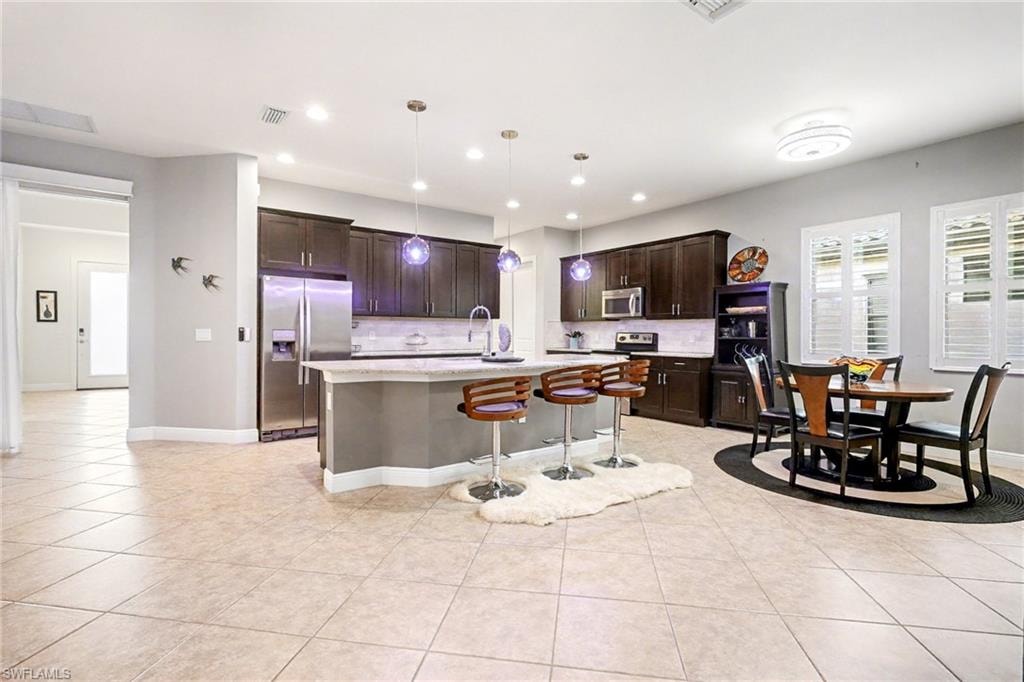 Kitchen featuring dark brown cabinetry, a breakfast bar, appliances with stainless steel finishes, pendant lighting, and a kitchen island with sink