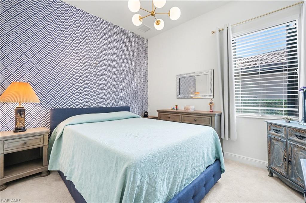 Bedroom featuring an accent wall, light carpet, a chandelier, and wallpapered walls