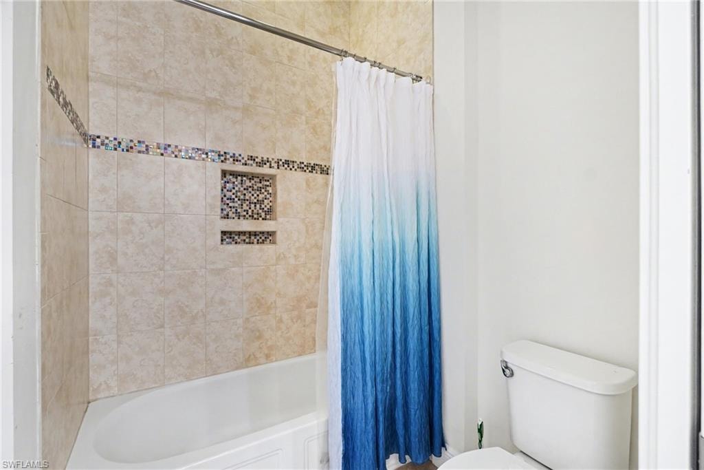 Full bathroom featuring shower / bath combination with curtain and toilet
