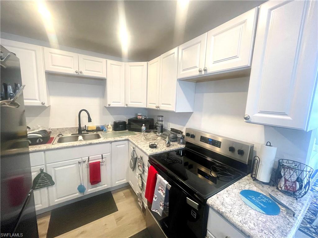 Kitchen with stainless steel electric stove, white cabinets, fridge, light wood-type flooring, and black microwave