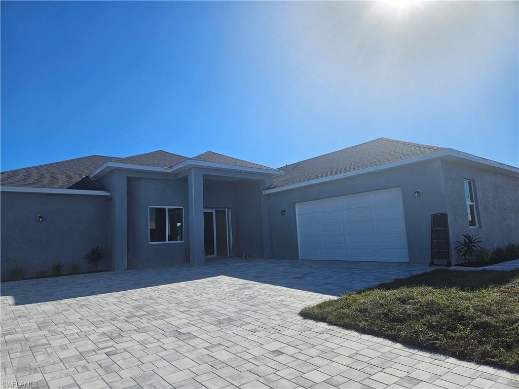 Ranch-style home featuring decorative driveway, stucco siding, an attached garage, and roof with shingles