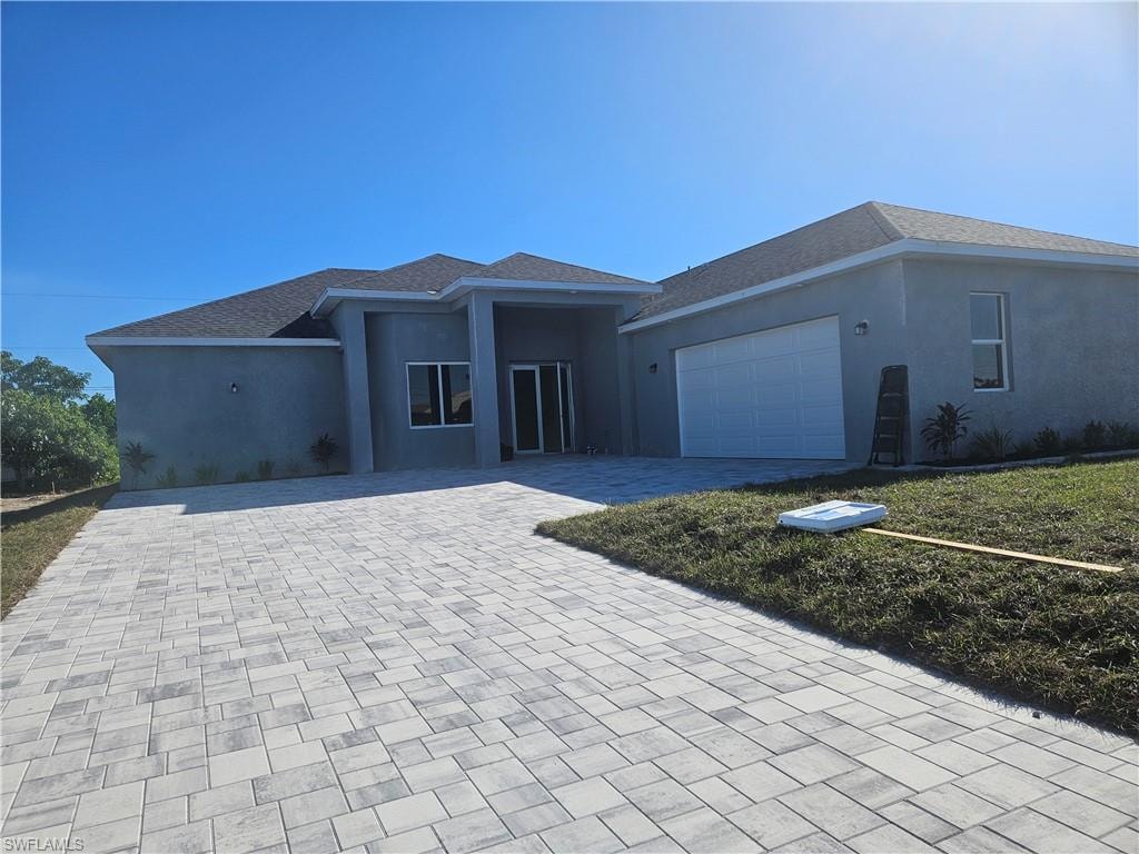 View of front of property with decorative driveway, stucco siding, an attached garage, and roof with shingles