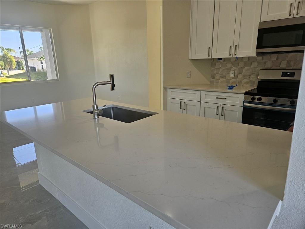 Kitchen featuring light stone countertops, stainless steel appliances, white cabinetry, and decorative backsplash