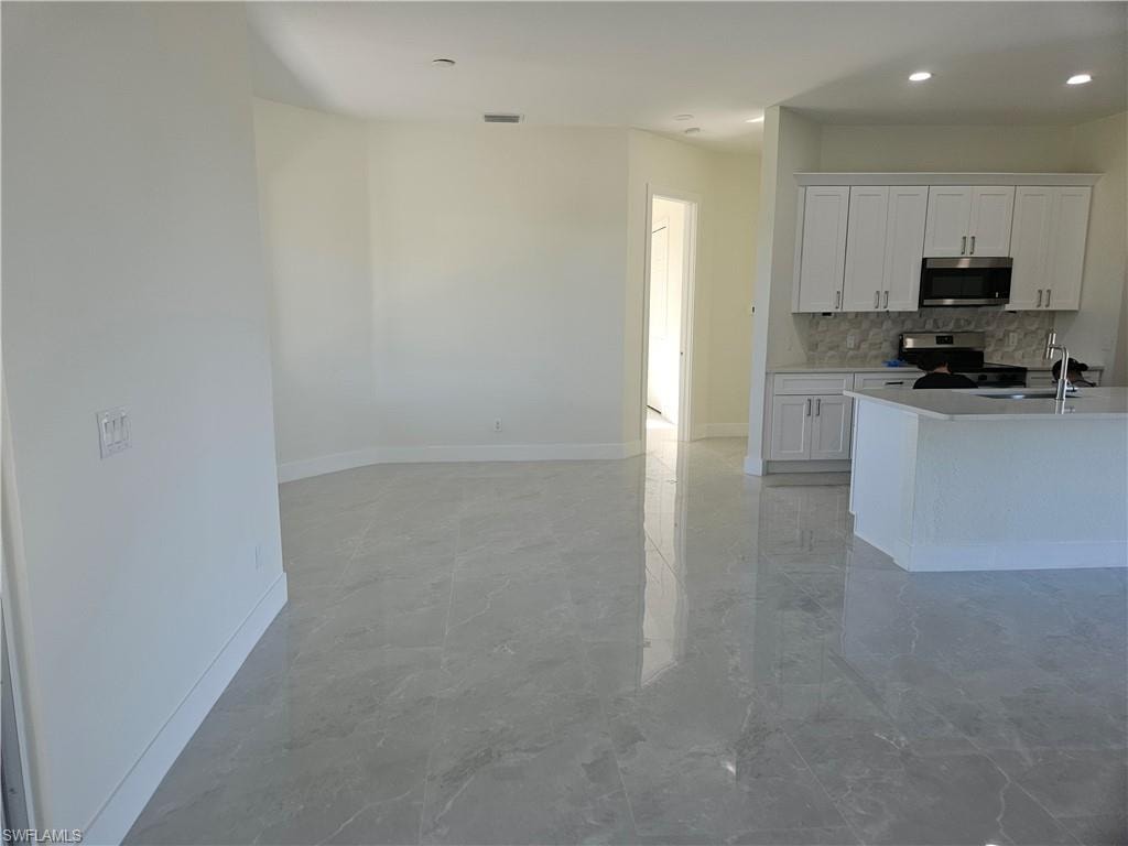 Kitchen with white cabinets, appliances with stainless steel finishes, tasteful backsplash, light marble finish floors, and recessed lighting