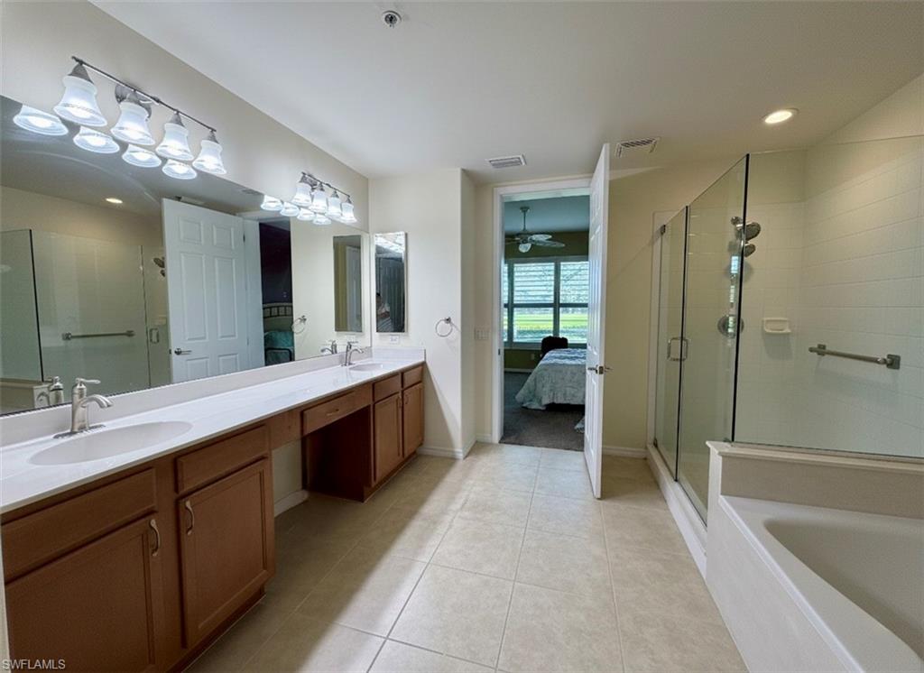 Ensuite bathroom featuring double vanity, light tile patterned floors, a garden tub, a shower stall, and ceiling fan *Photos have been virtually staged for perspective.