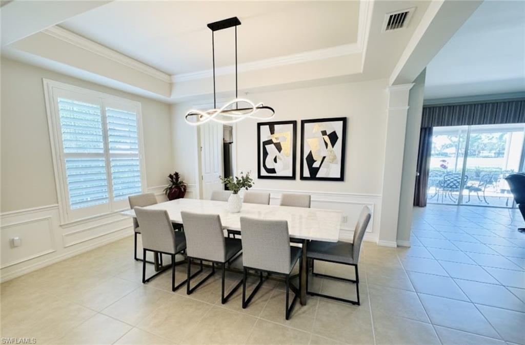 Dining area with a decorative wall, a wainscoted wall, ornamental molding, light tile patterned floors, and a raised ceiling. *Photos have been virtually staged for perspective.