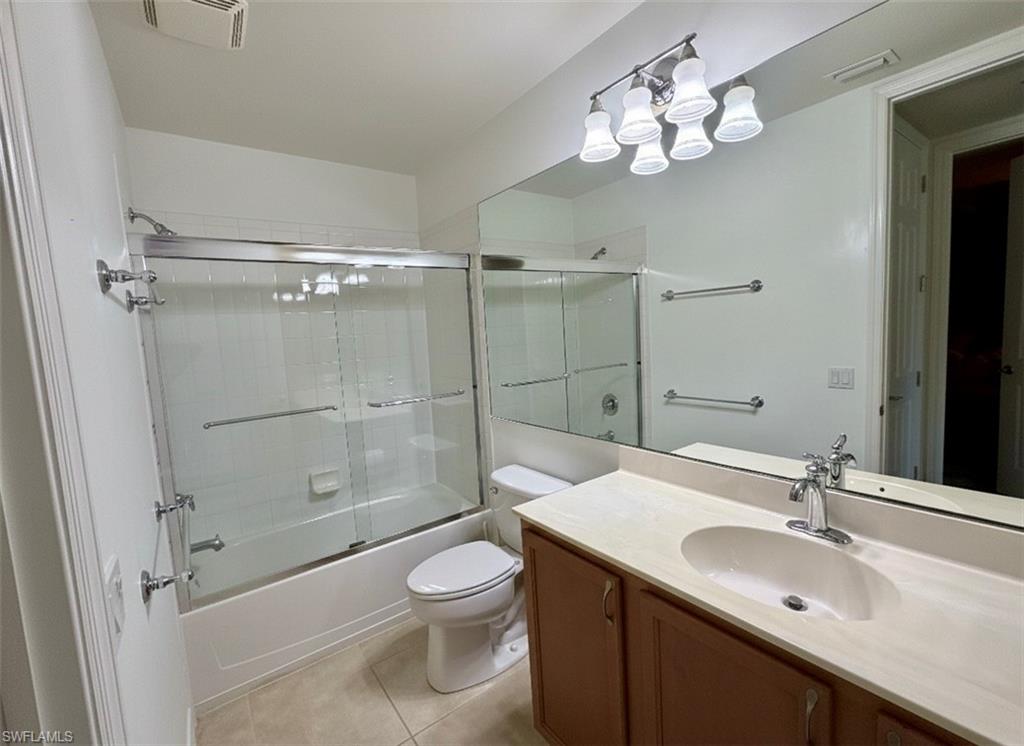 Bathroom with combined bath / shower with glass door, vanity, and light tile patterned floors*Photos have been virtually staged for perspective.