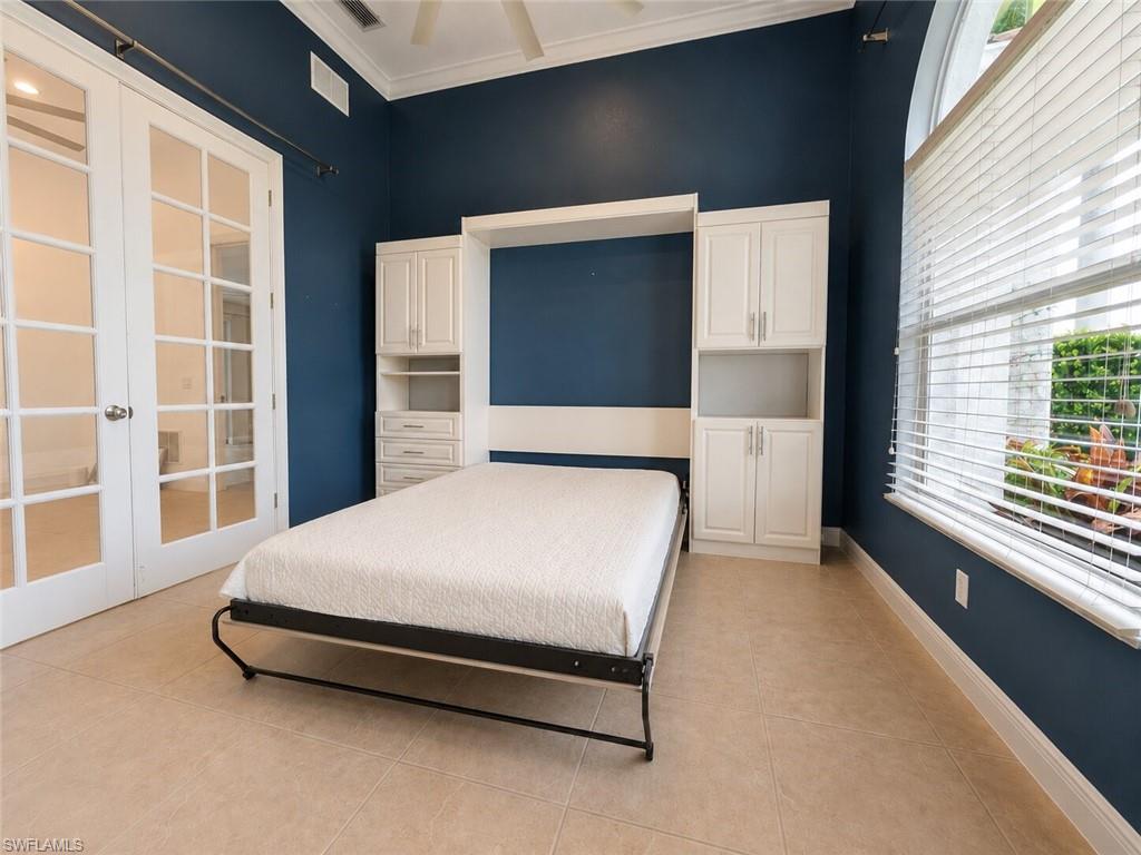 Office featuring a built-in Murphy bed system with integrated cabinetry and shelving, large arched window with blinds, French doors, tile flooring, and a vaulted ceiling with a ceiling fan