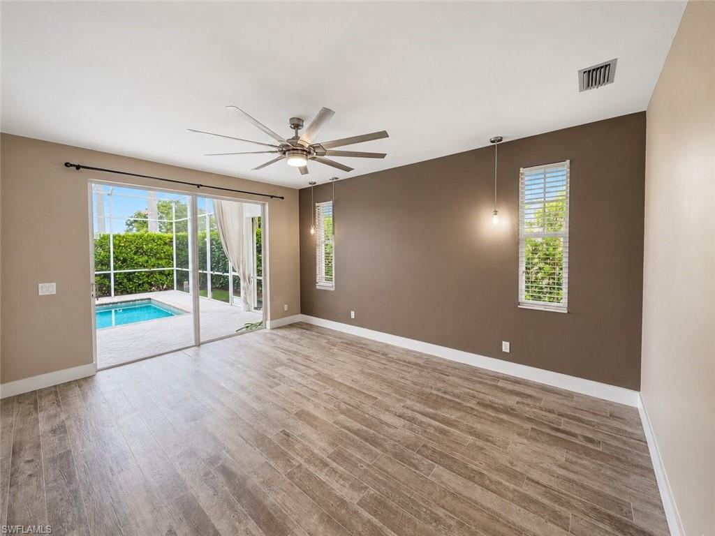 Spacious room featuring wood-finish flooring, a large sliding glass door opening to a screened patio with a pool, and two windows with blinds