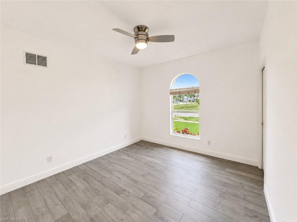 Neutral-toned interior featuring wood-finish flooring, a contemporary ceiling fan with integrated lighting, and a prominent arched window