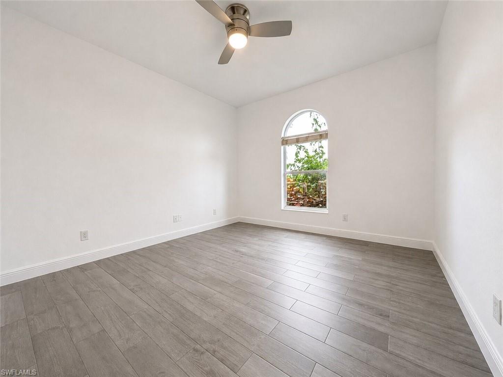 Spacious room featuring vaulted ceilings, light wood-finish flooring, a contemporary ceiling fan, and an arched window