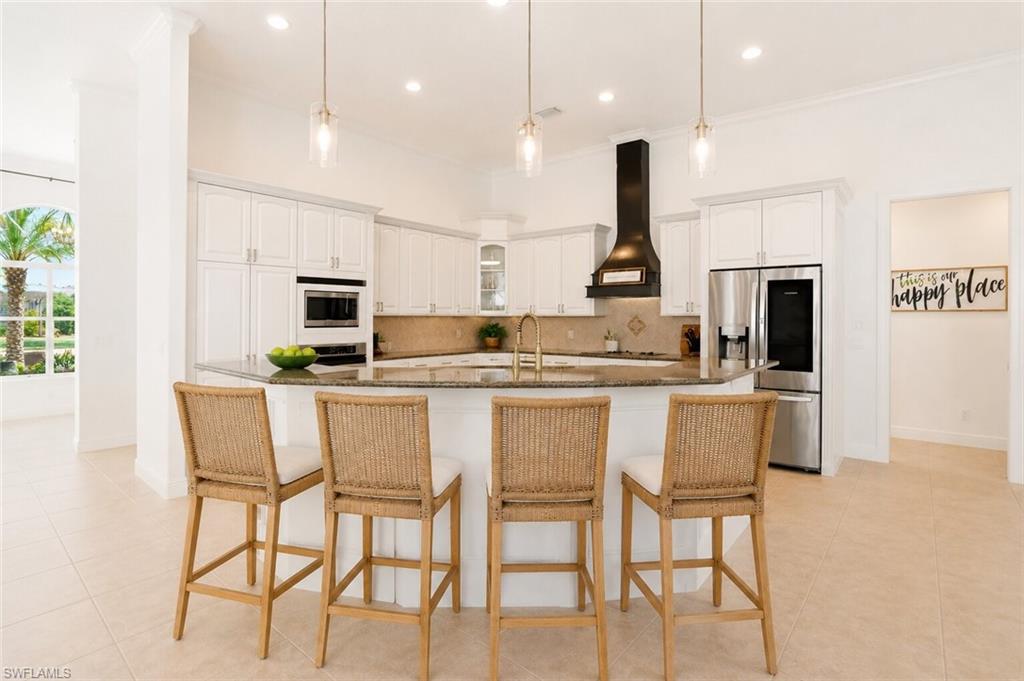 Kitchen featuring a curved island with stone countertop, white cabinetry with crown molding, stainless steel appliances, and a black range hood