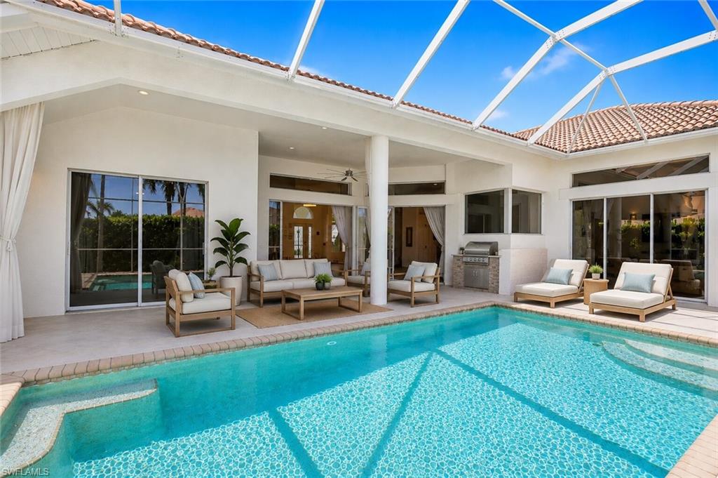Expansive screened lanai featuring a sparkling pool with integrated steps, a covered patio area, an outdoor built-in grill station, and multiple large sliding glass doors