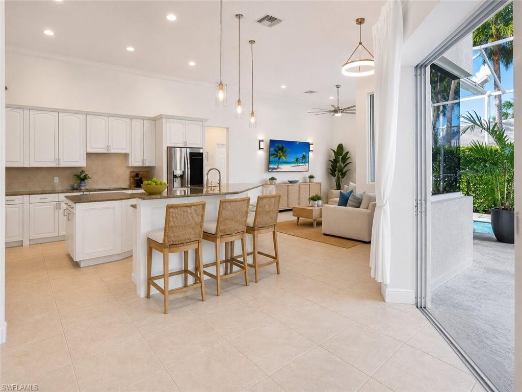 Contemporary open-concept kitchen and living area featuring a large center island with seating, a stainless steel refrigerator, white cabinetry, and tile flooring