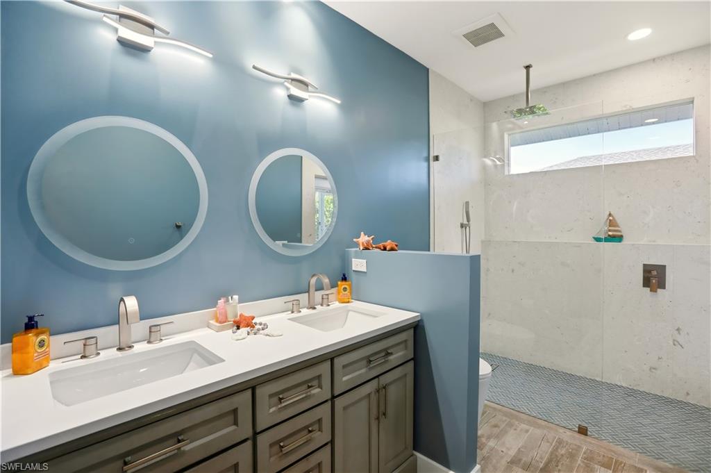 Bathroom featuring a walk in shower, double vanity, and light wood-style flooring