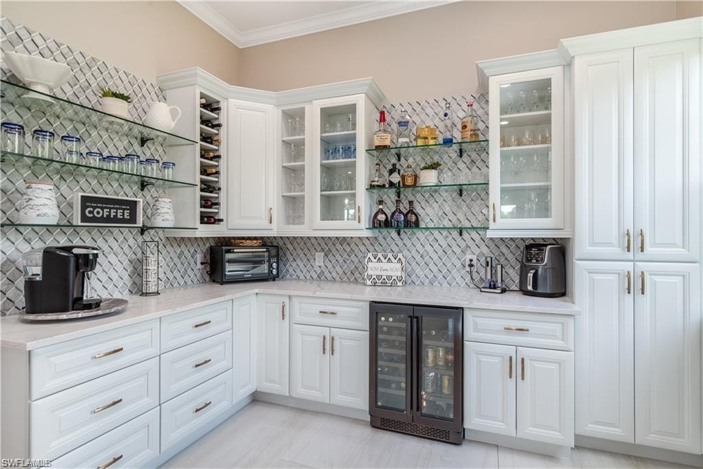 Bar area with open shelves, beverage cooler, ornamental molding, glass insert cabinets, and light stone counters
