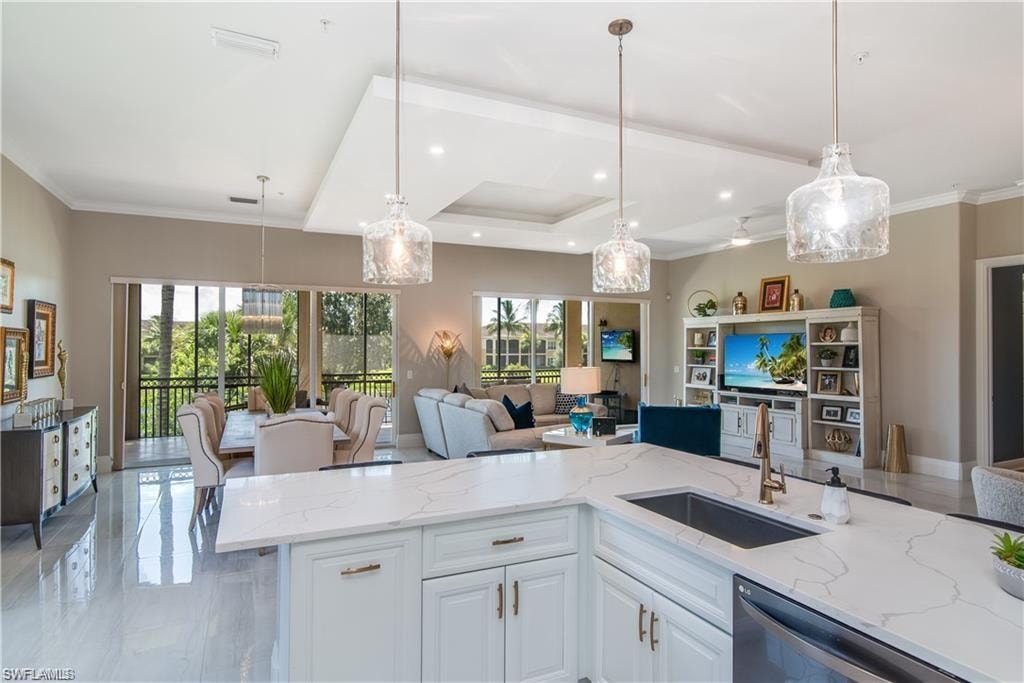 Kitchen featuring light stone countertops, open floor plan, white cabinets, decorative light fixtures, and ornamental molding