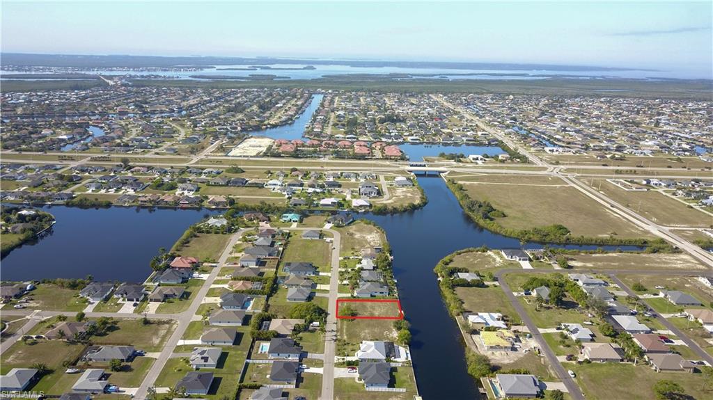 Aerial view of property and surrounding area featuring nearby suburban area, property parcel outlined, and a nearby body of water