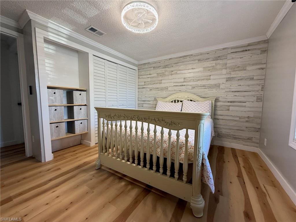 Bedroom with wood walls, a textured ceiling, crown molding, light wood-style floors, and a closet