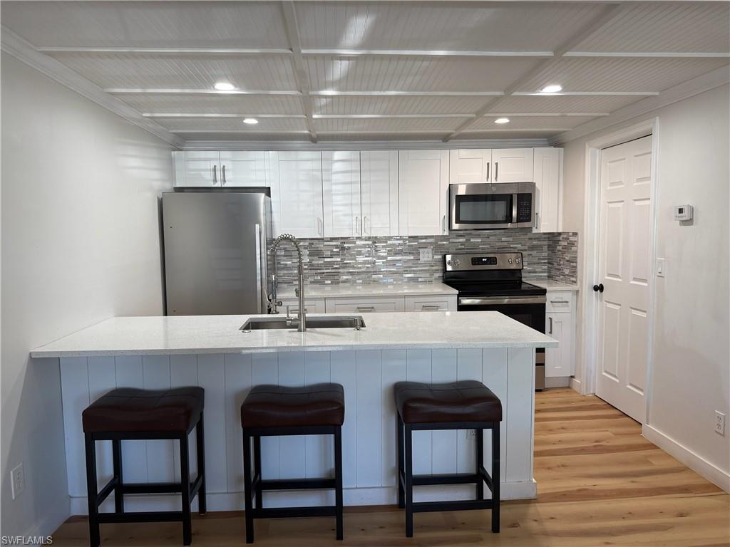 Kitchen with  breakfast bar, stainless steel appliances, white cabinets, and light stone countertops
