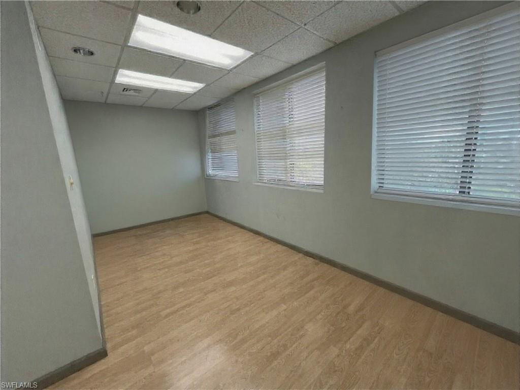 Spacious room featuring wood-finish flooring, multiple windows with blinds, recessed lighting, and fluorescent panel lighting