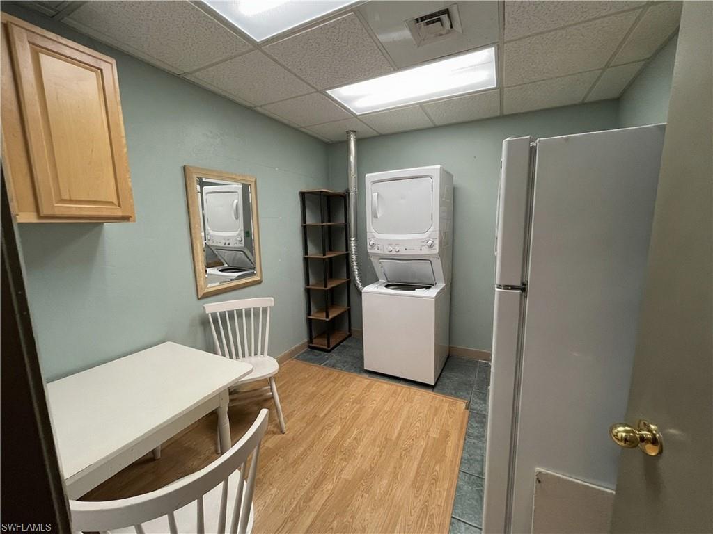 Compact utility space featuring a stacked washer and dryer unit, wood-finish flooring, and a drop ceiling with fluorescent lighting