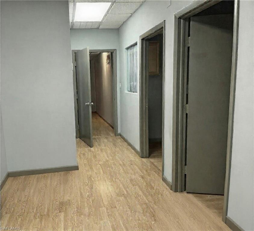 Hallway featuring wood-finish flooring, light grey walls, and multiple doorways with dark trim