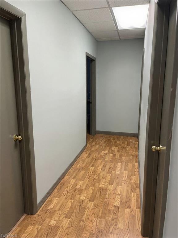 Hallway featuring wood-finish flooring, light gray walls, dark trim, and a drop ceiling with recessed lighting