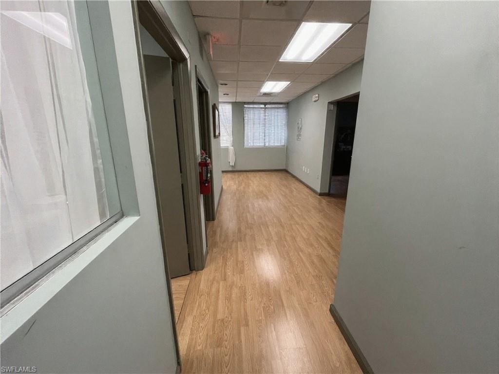 Hallway featuring wood-finish flooring, recessed fluorescent lighting, light-toned wall paint, and multiple doorways