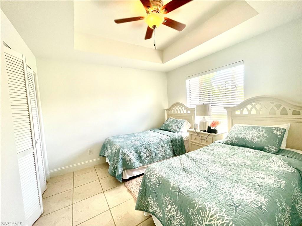 Bedroom with a raised ceiling, light tile patterned floors, ceiling fan, and a closet