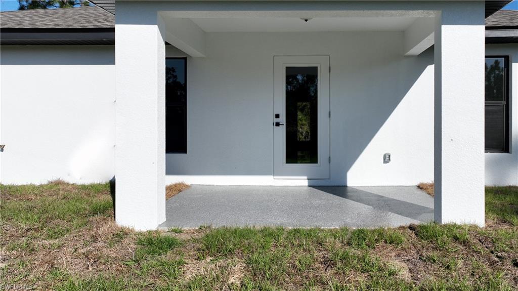 View of exterior entry featuring a shingled roof, a patio, and stucco siding