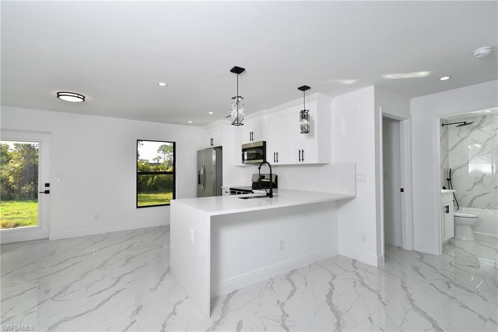 Kitchen with stainless steel appliances, a peninsula, pendant lighting, white cabinets, and light stone countertops