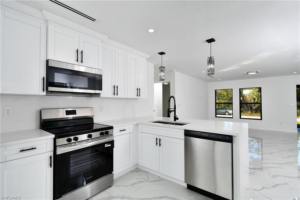 Kitchen with stainless steel appliances, light stone countertops, pendant lighting, a peninsula, and white cabinetry