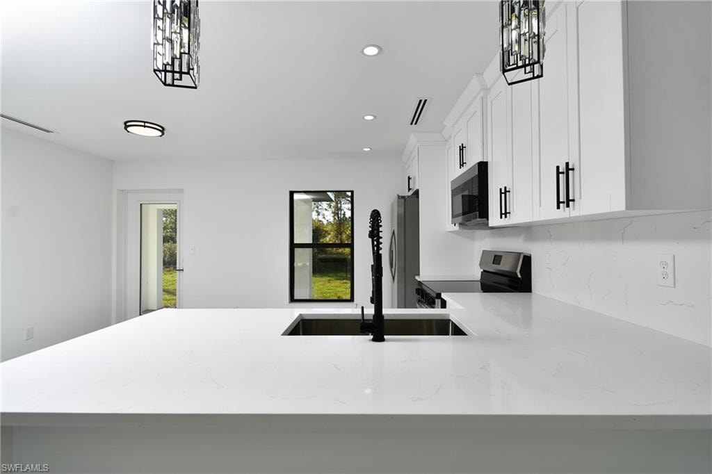 Kitchen featuring light stone countertops, stainless steel appliances, white cabinetry, a peninsula, and pendant lighting