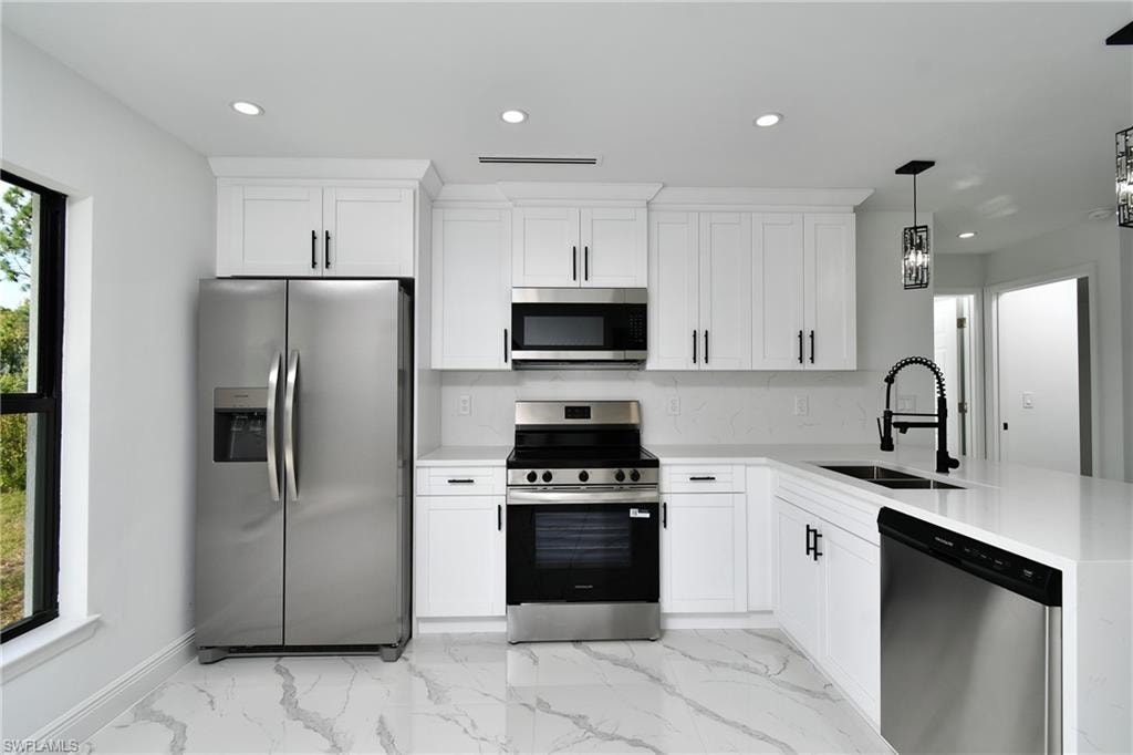 Kitchen with stainless steel appliances, hanging light fixtures, light stone countertops, and white cabinets