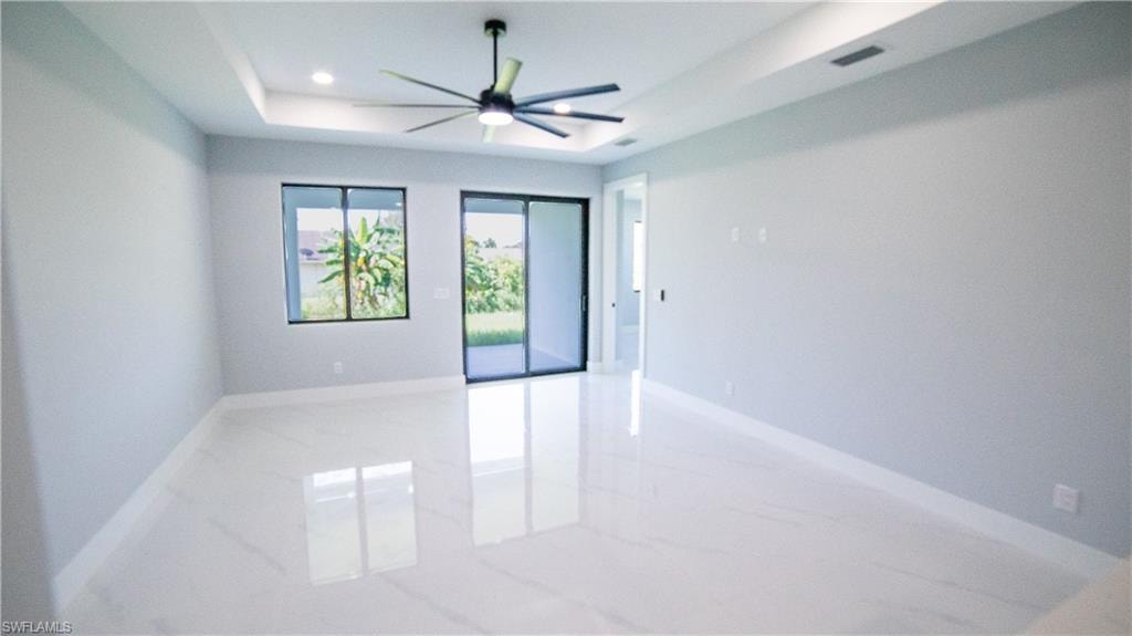 Spare room featuring light marble finish flooring, a raised ceiling, a ceiling fan, and recessed lighting