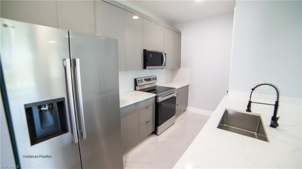 Kitchen featuring stainless steel appliances, modern cabinets, gray cabinets, light stone counters, and recessed lighting