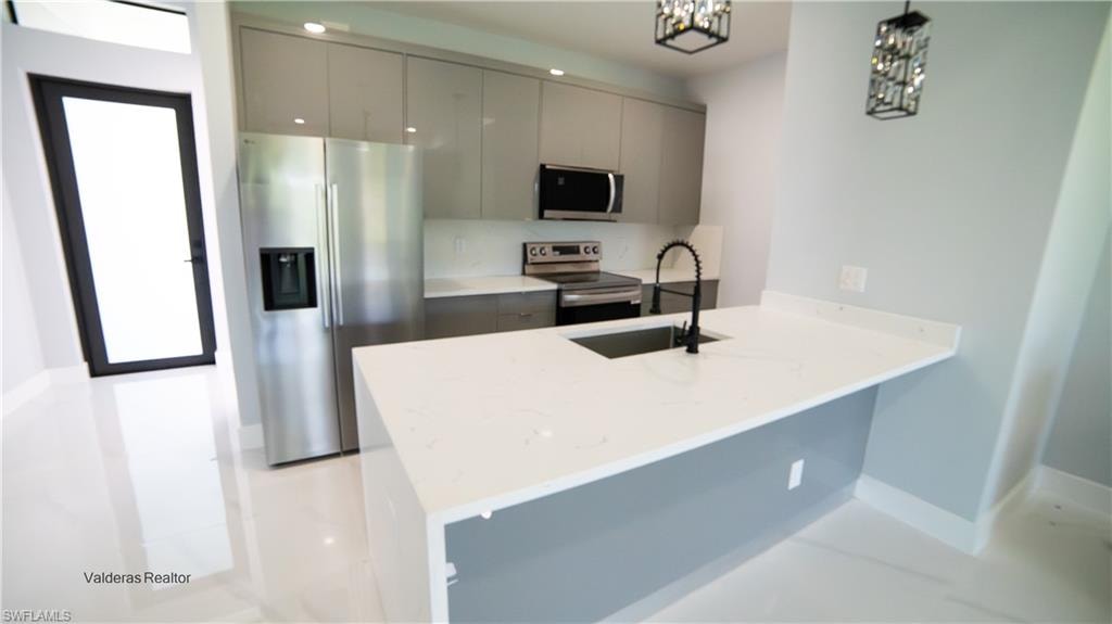 Kitchen with stainless steel appliances, modern cabinets, light stone counters, a peninsula, and hanging light fixtures