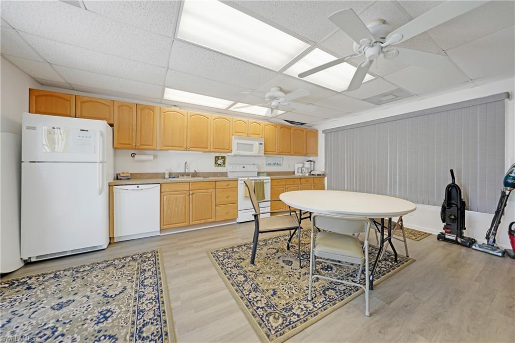 Kitchen with white appliances, light countertops, light brown cabinets, ceiling fan, and a drop ceiling