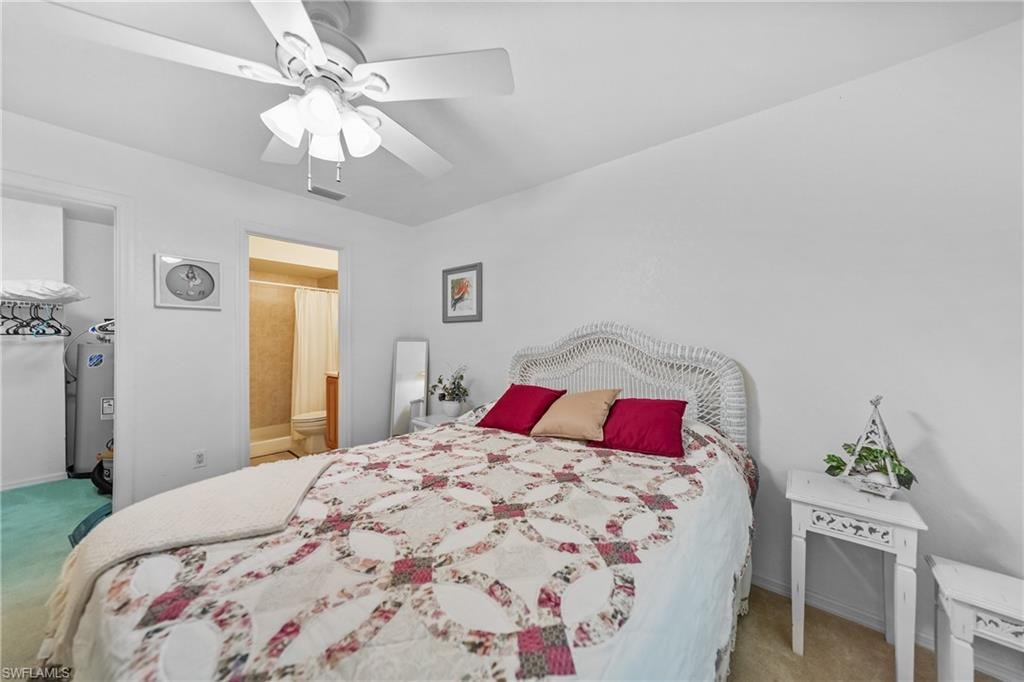 Bedroom featuring light carpet, ceiling fan, water heater, and ensuite bath