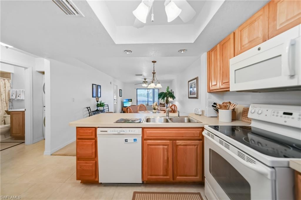 Kitchen with white appliances, ceiling fan, a peninsula, light countertops, and a raised ceiling