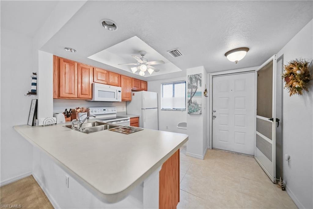 Kitchen with a peninsula, white appliances, light countertops, ceiling fan, and light tile patterned floors