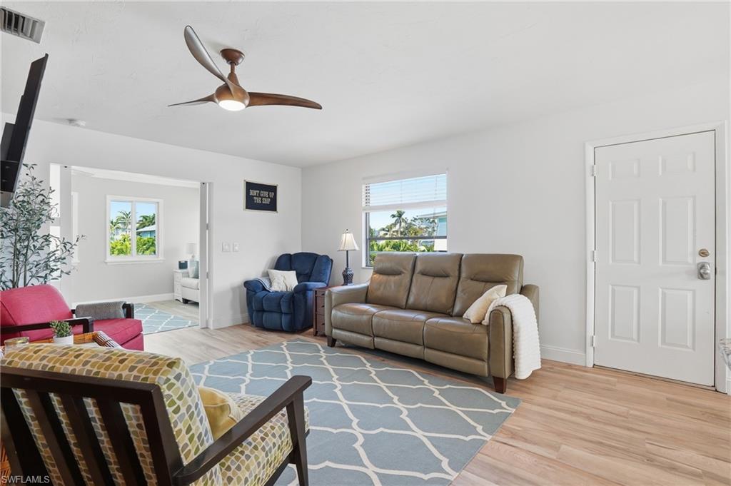 Living area with light wood-style floors, a ceiling fan, and plenty of natural light - Virtually Edited Image