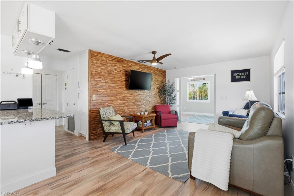 Living room with ceiling fan, light wood finished floors, and an accent wall - Virtually Edited Image