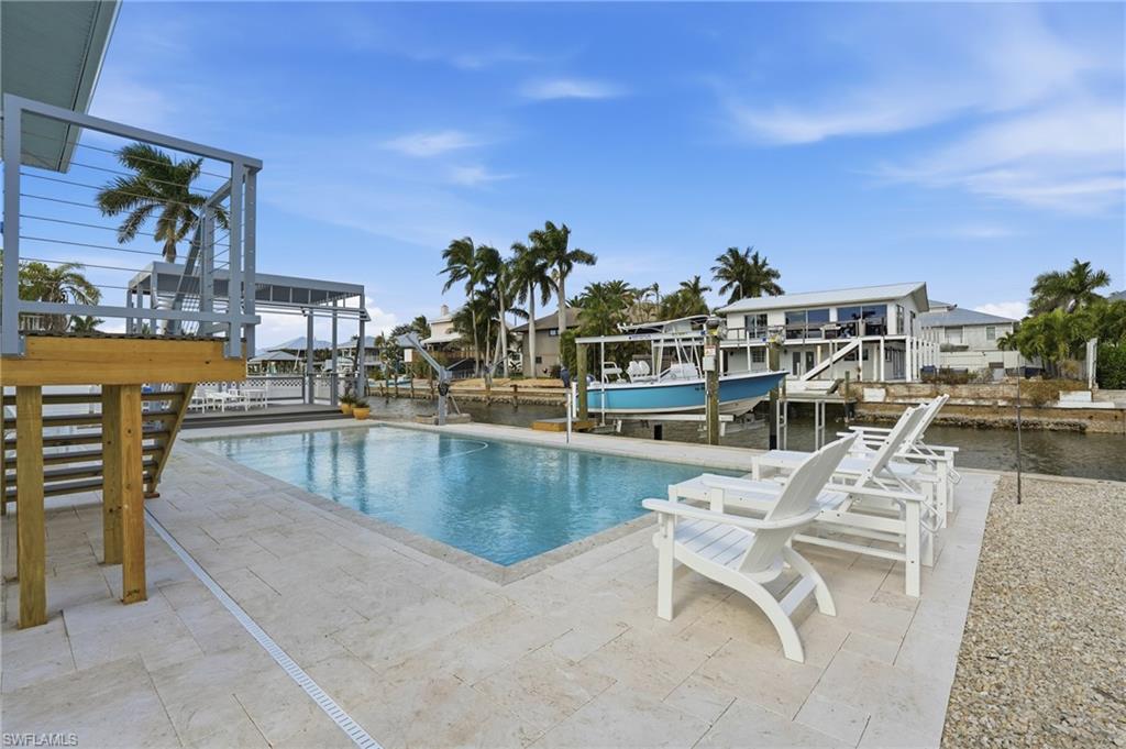 Swimming pool with boat lift, a dock, a patio, and a water view - Virtually Edited Image