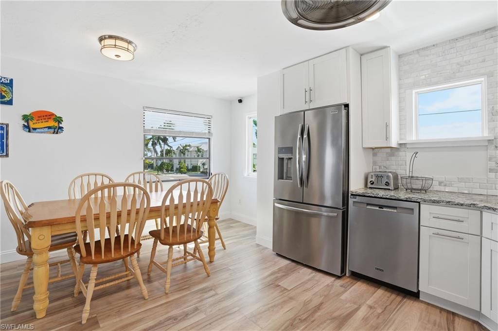 Kitchen with stainless steel appliances, white cabinets, light stone countertops, backsplash, and light wood-style flooring - Virtually Edited Image