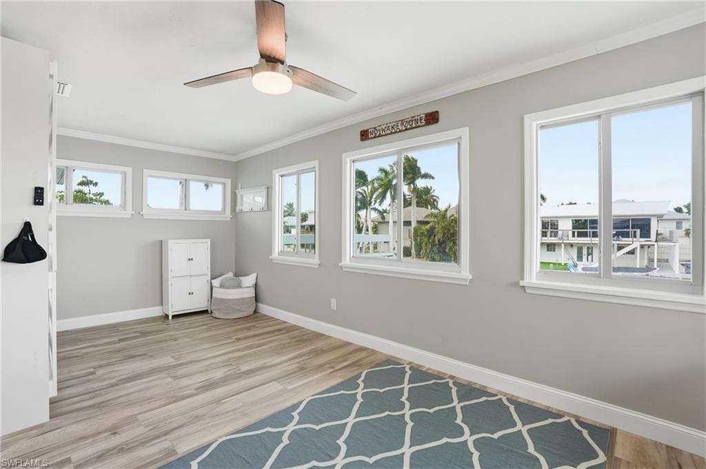 Den featuring a ceiling fan, multiple windows, light wood-style flooring, and crown molding - Virtually Edited Image