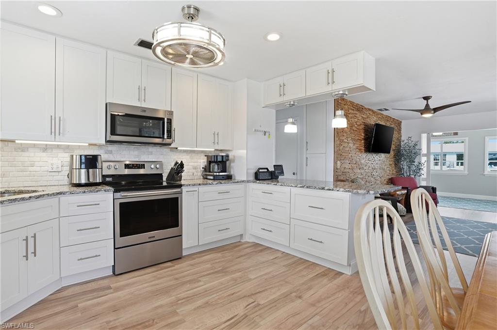 Kitchen with white cabinetry, appliances with stainless steel finishes, a ceiling fan, light stone countertops, and light wood-type flooring - Virtually Edited Image