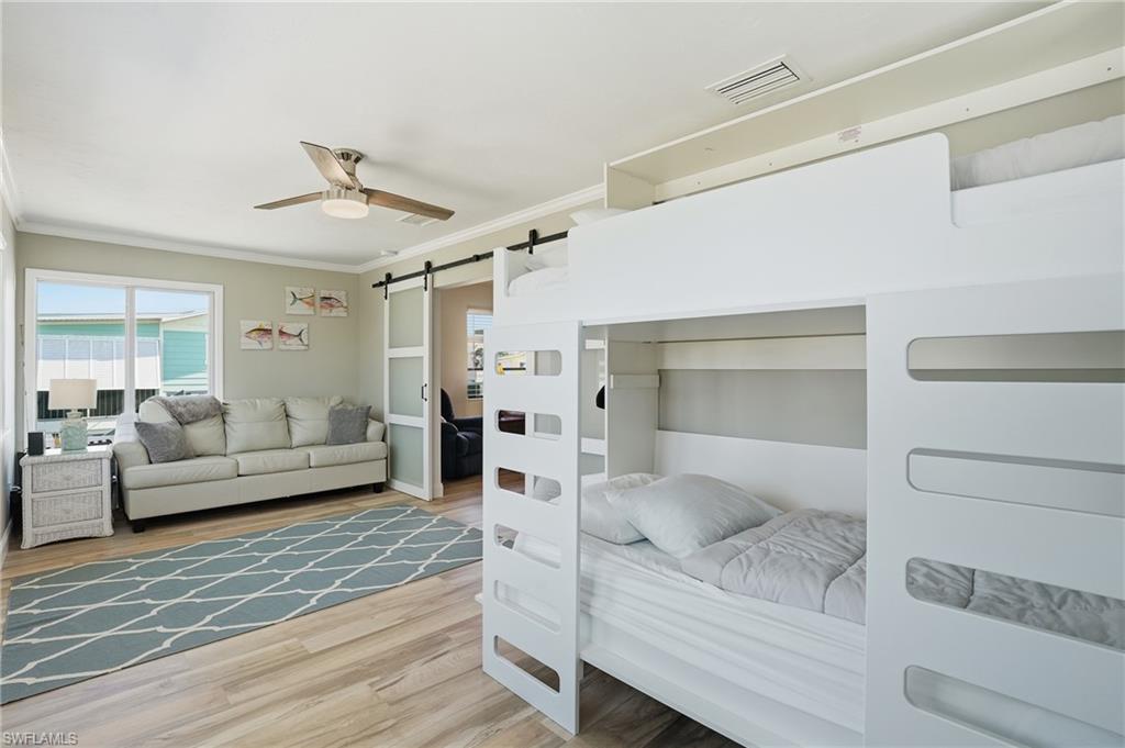 Den with a barn door, crown molding, ceiling fan, and wood finished floors - Virtually Edited Image
